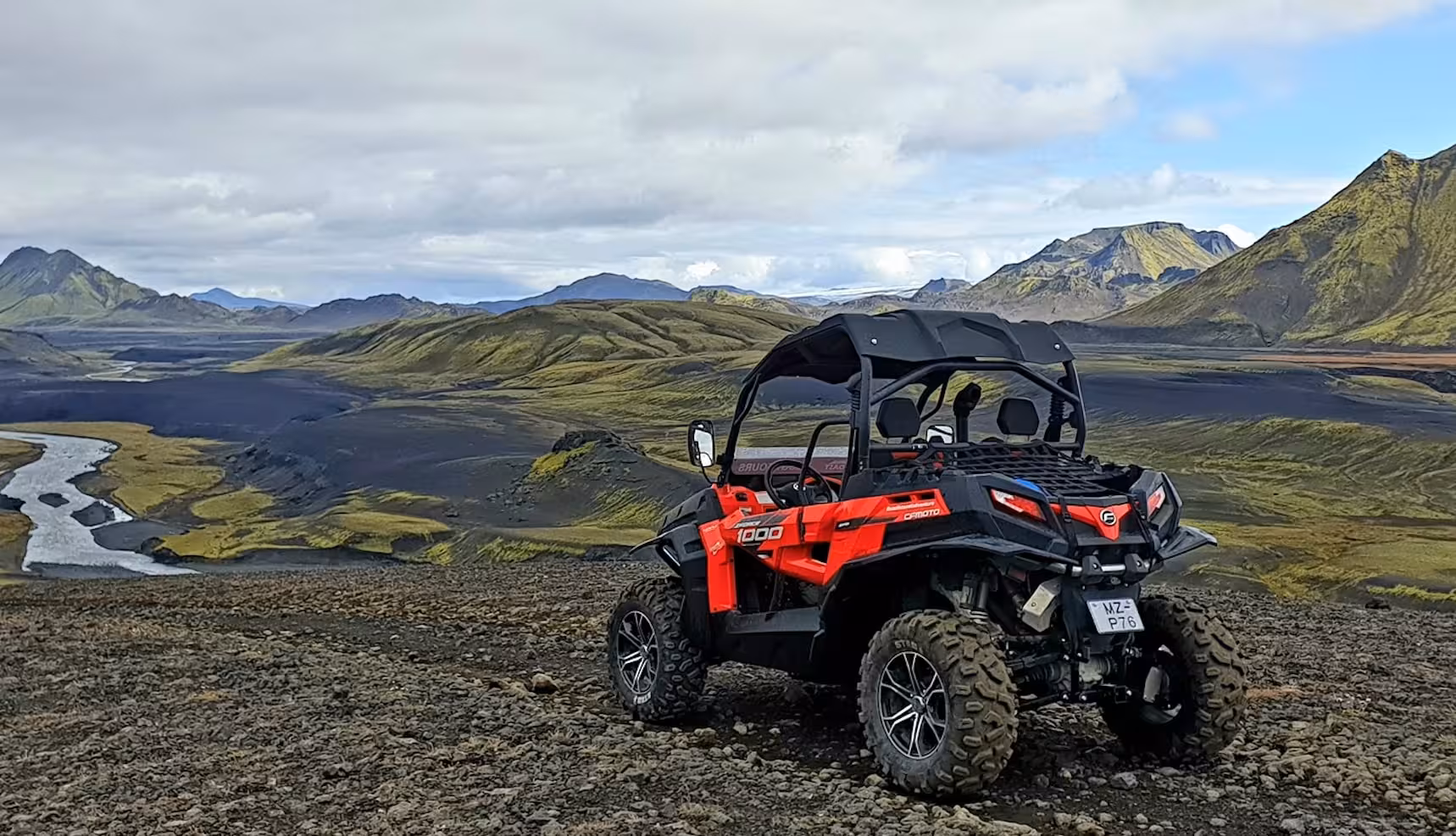 Red CFMOTO 1000 buggy parked on rocky highland terrain with green moss-covered mountains and river valley in Iceland