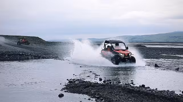 Red buggy ATV splashing through shallow river on rocky Iceland off-road terrain