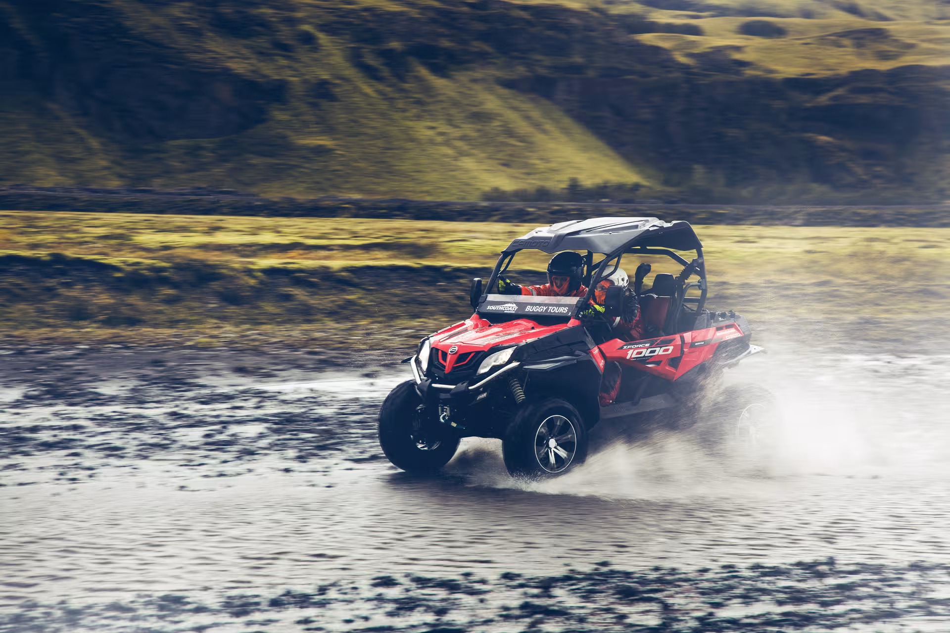 Red CFMOTO ZForce 1000 buggy splashing through a shallow river in Iceland's green highlands