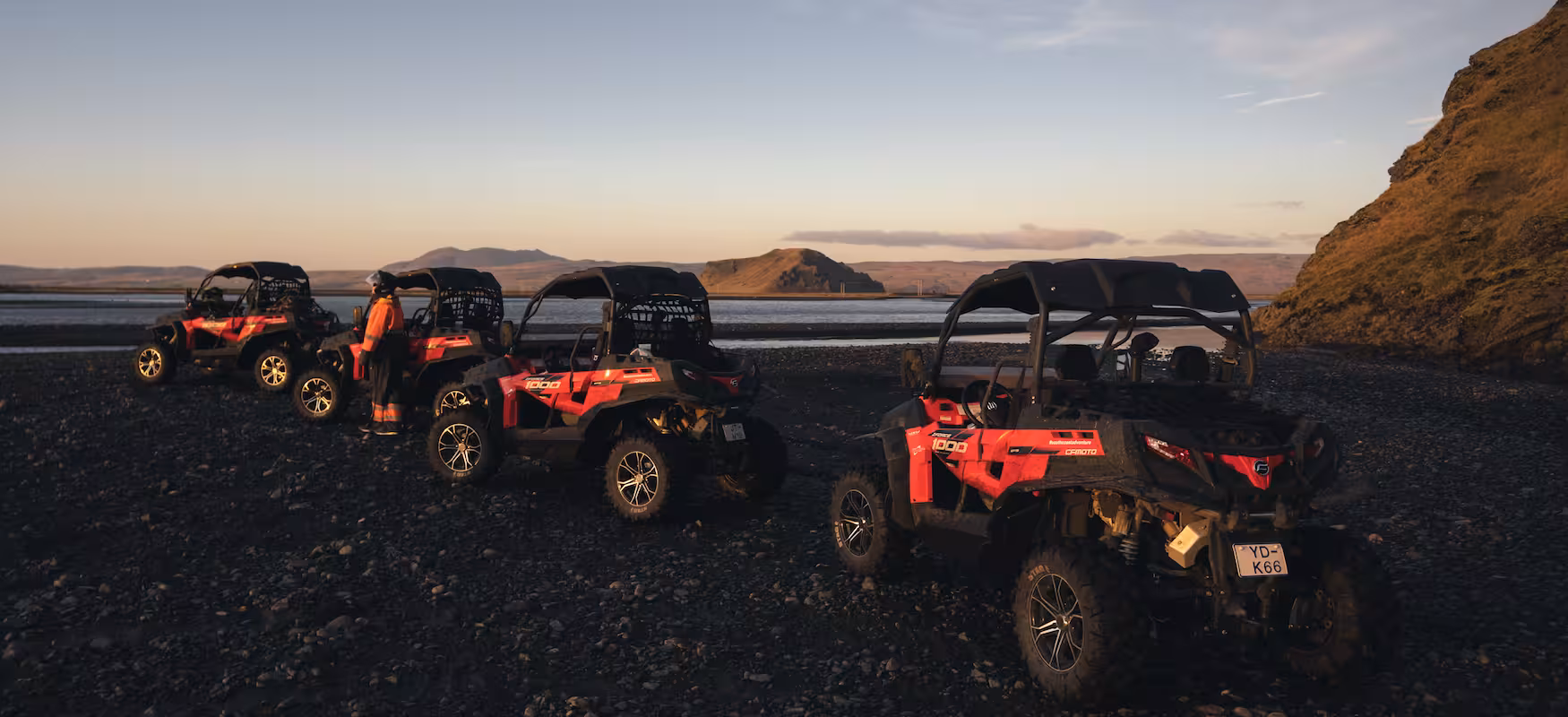 Three red CFMOTO 1000 off-road buggies parked on Iceland's black sand beach at sunset with mountains in background