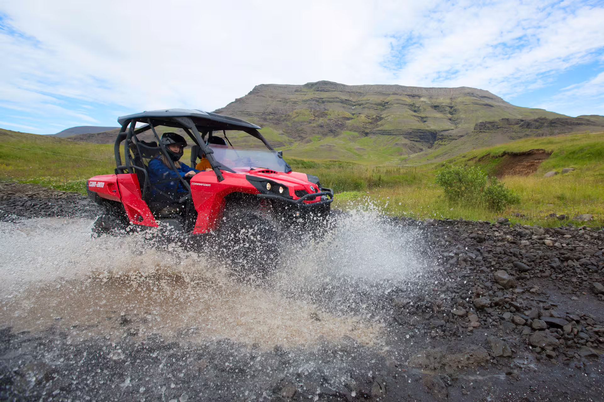Red buggy splashes through water on a thrilling 1-hour safari adventure in stunning mountainous terrain under blue skies.