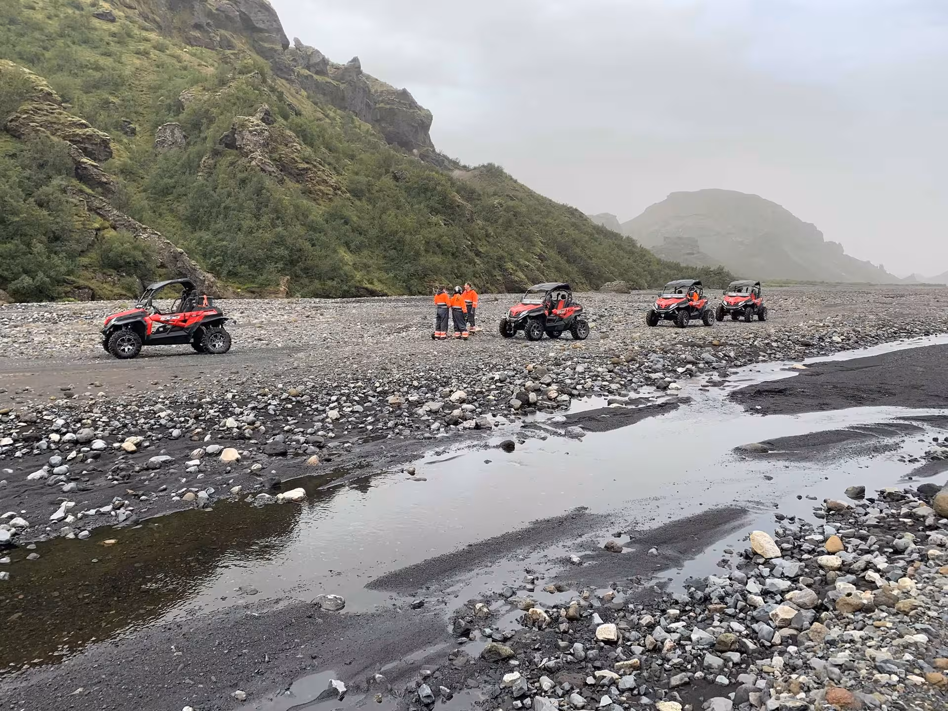 Red off-road buggies parked on rocky Icelandic riverbed with green volcanic mountains in background