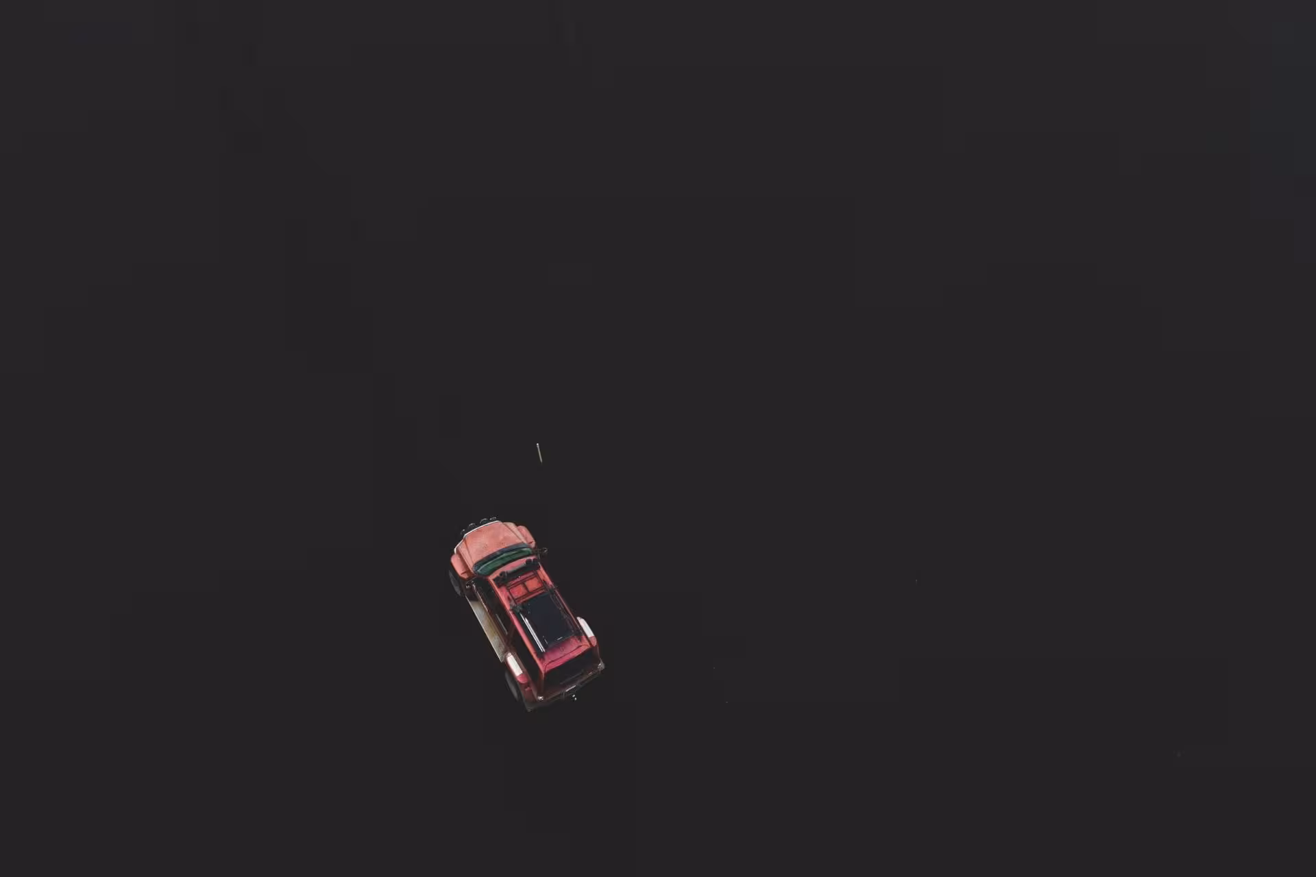 Aerial view of a red vehicle driving through dark Landmannalaugar highlands terrain