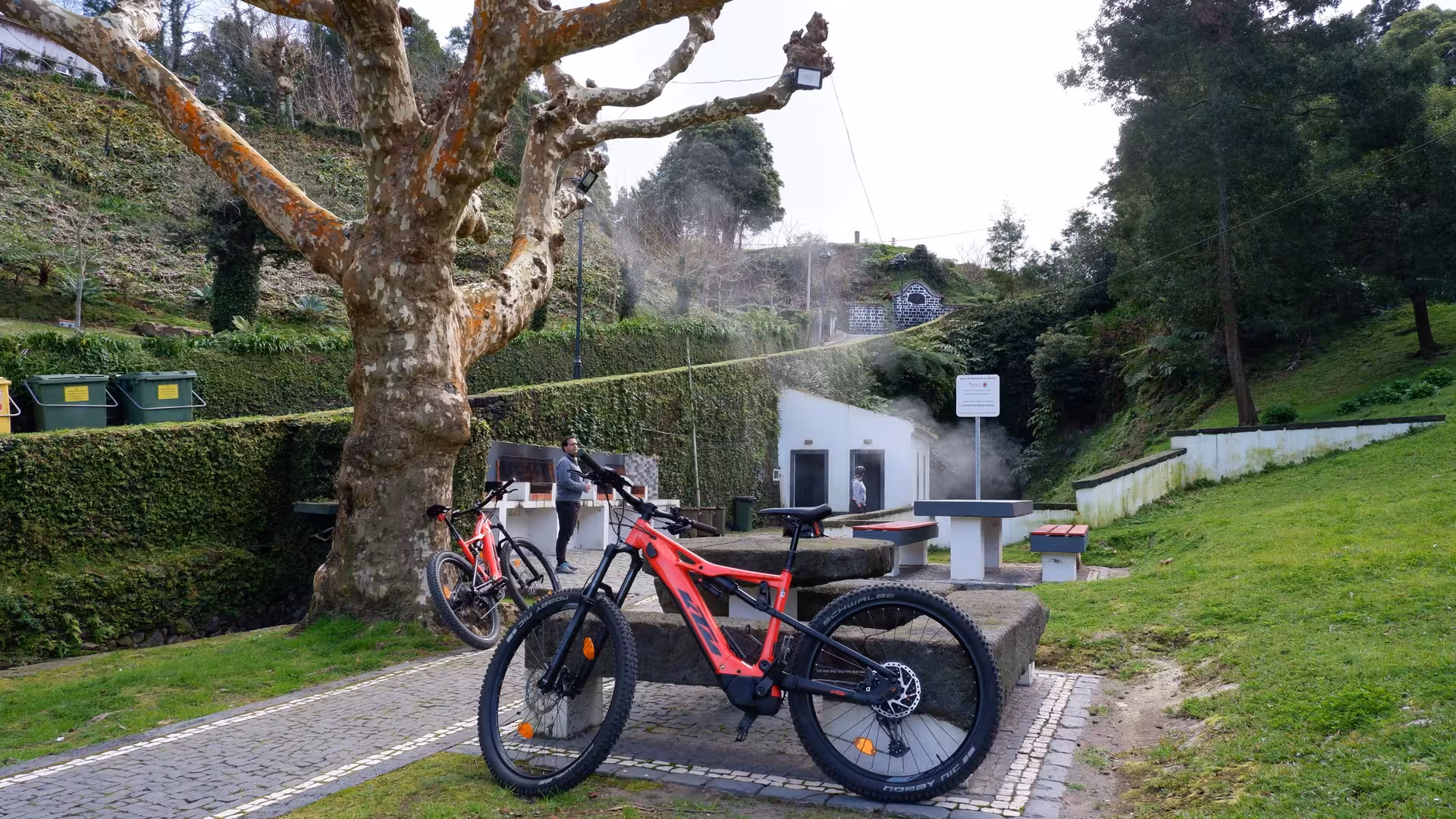 Red e-bike parked by hot springs and lush green hills on a guided Ribeira Grande cycling tour in São Miguel, Azores