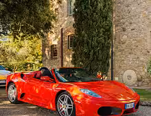Red Ferrari F430 Spider supercar parked in front of a stone building in Tuscany