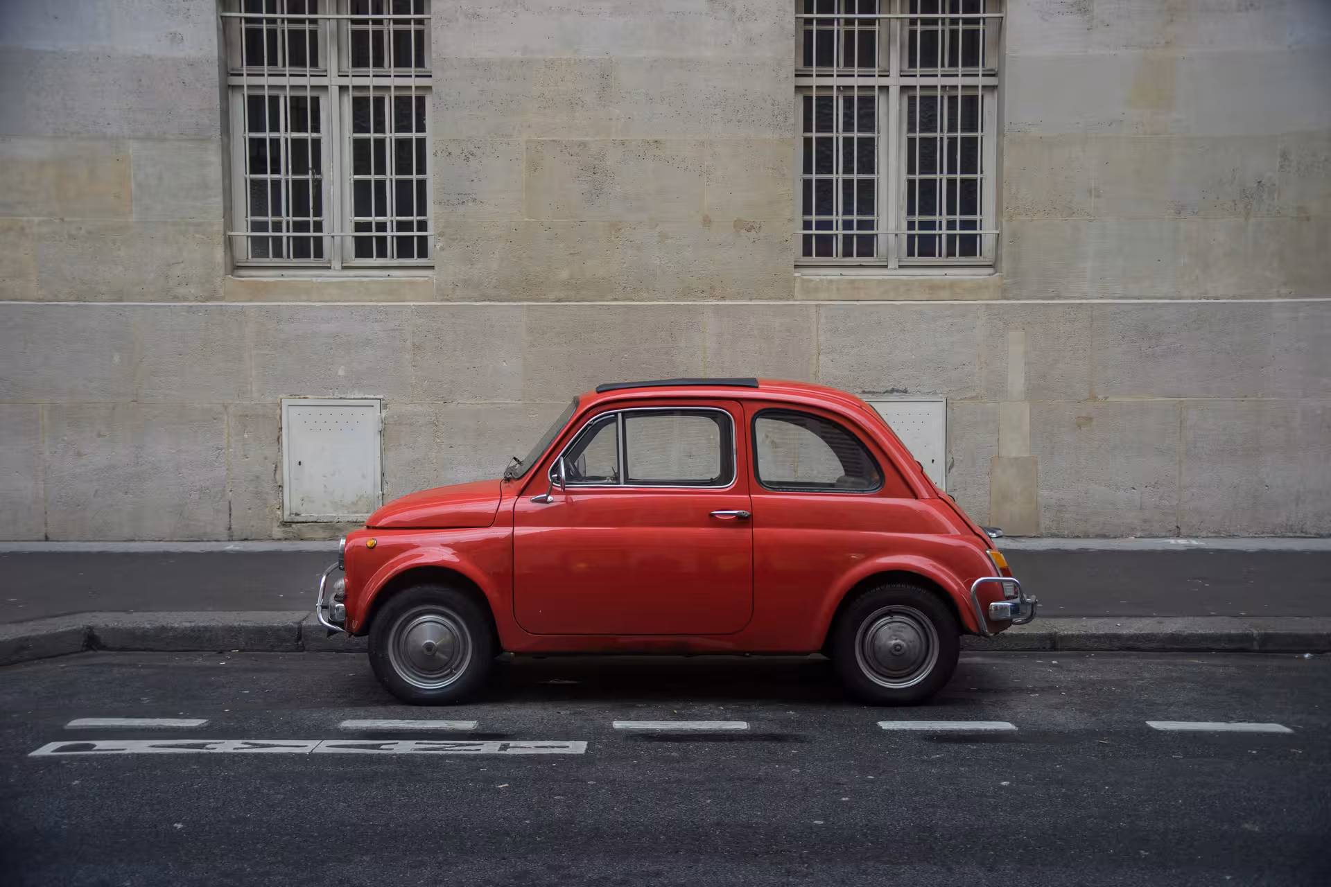 Classic red Fiat '500 parked against a stone wall, featured in The Roman Hills Vintage Tour by Fiat '500.