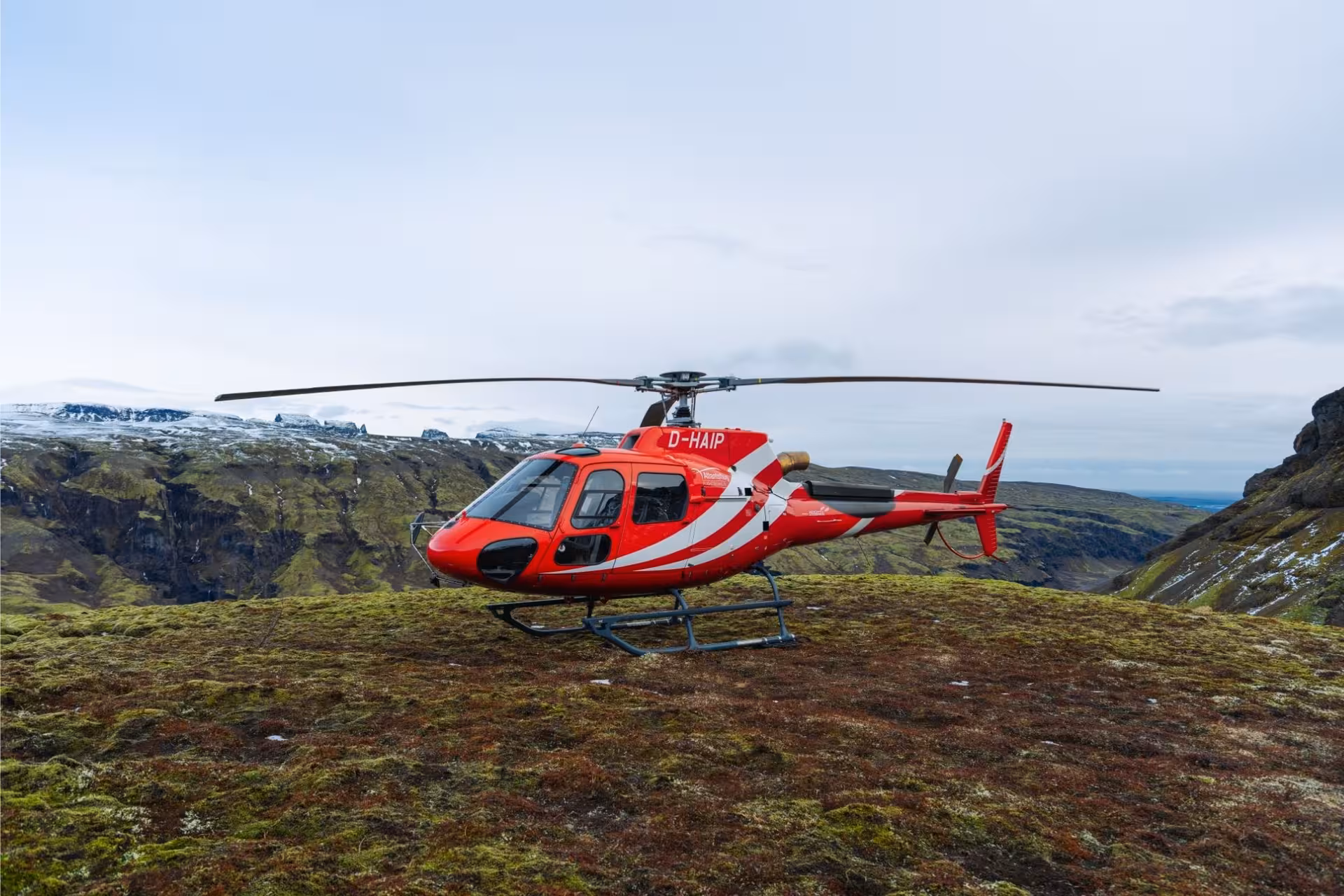 Red helicopter with registration D-HAIP landed on mossy highland terrain in Iceland with glacier and mountains in background