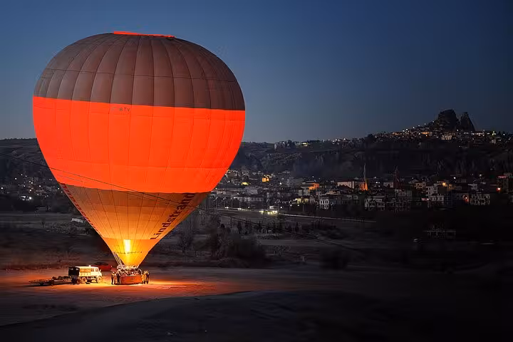 Red hot air balloon preparing for takeoff at sunrise in Cappadocia, overlooking Göreme town and valleys
