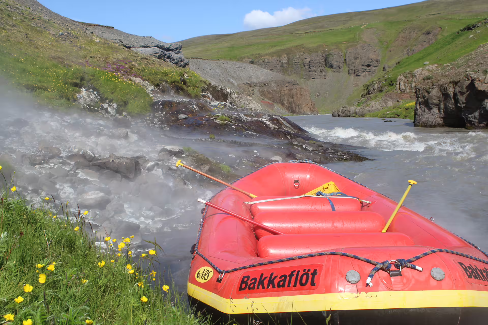 Red inflatable raft on a scenic riverbank surrounded by lush greenery, ideal for family river rafting adventures.