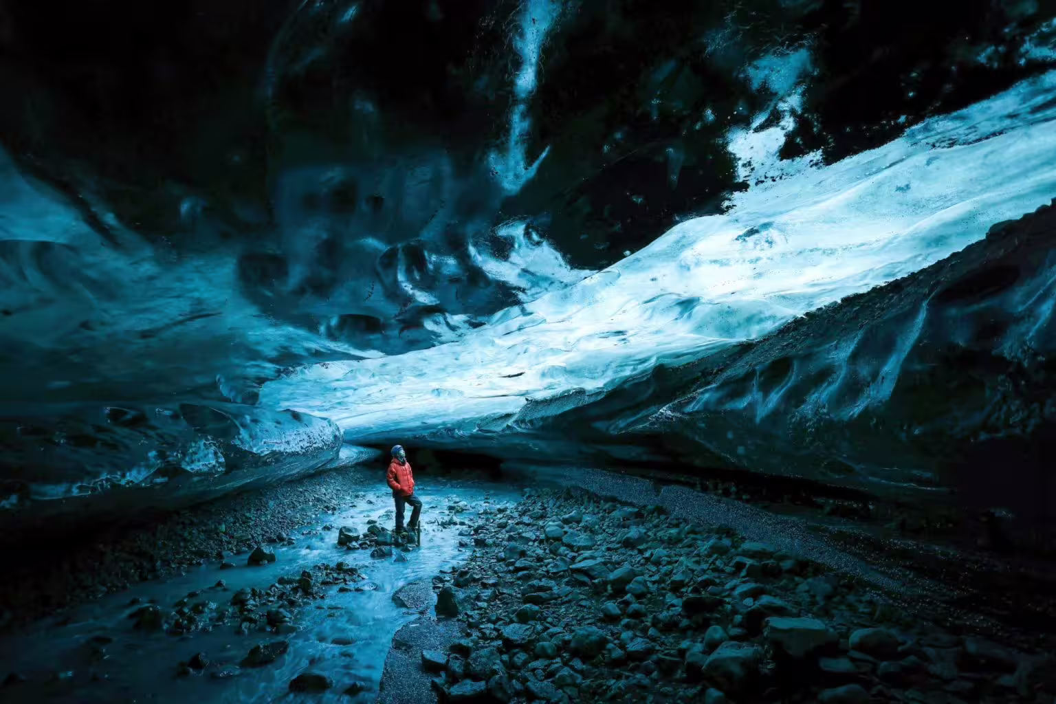 Solo explorer in red jacket standing inside a stunning blue glacial ice cave on a private photography tour in Iceland