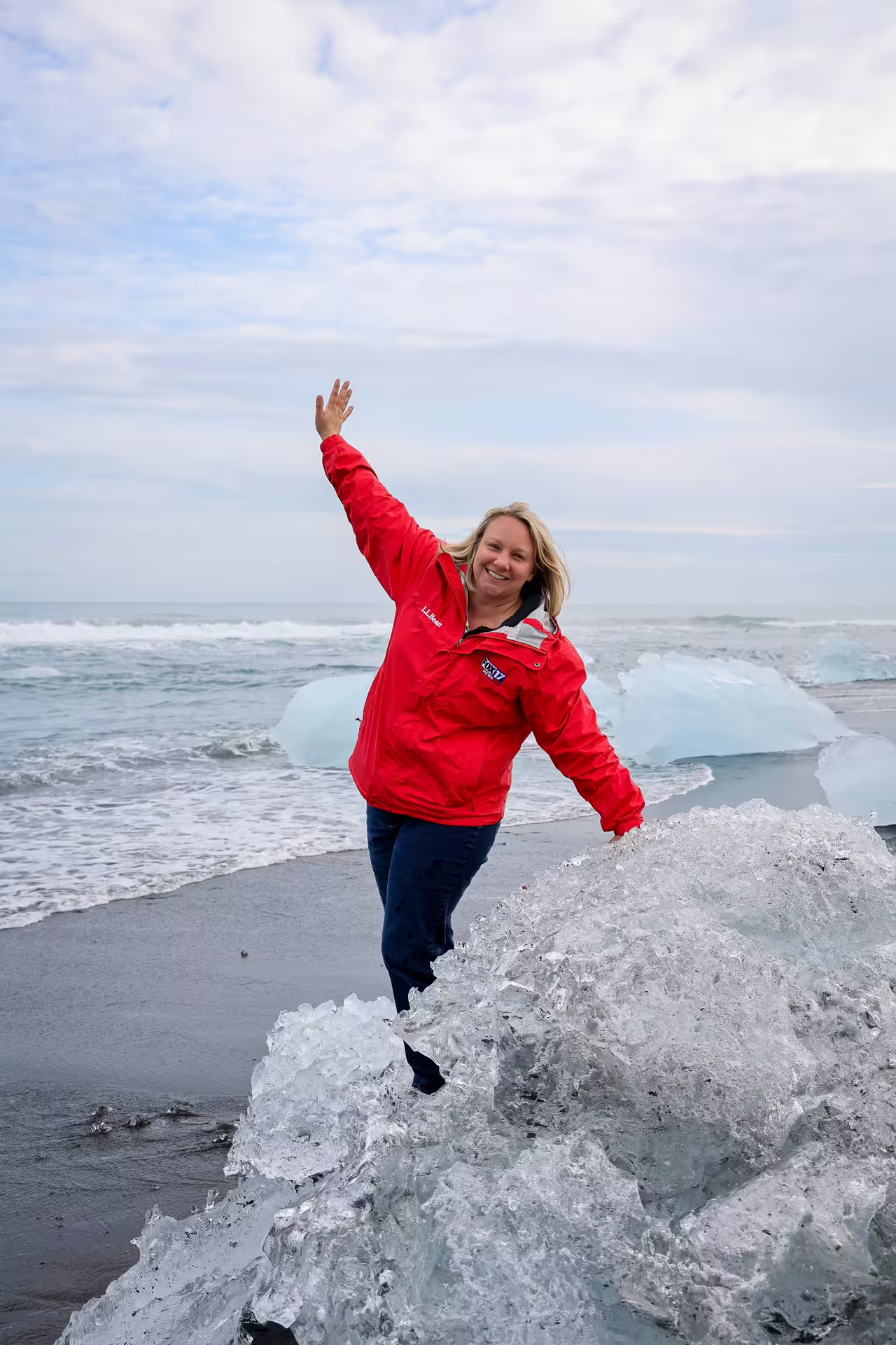 Joyful traveler in red jacket posing on glacier ice diamonds at Diamond Beach Iceland black sand shore