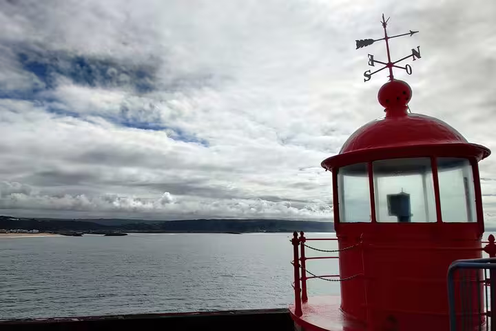 Red lighthouse with a weather vane overlooking the ocean, seen during a private transfer from Lisbon to Porto with scenic stops.