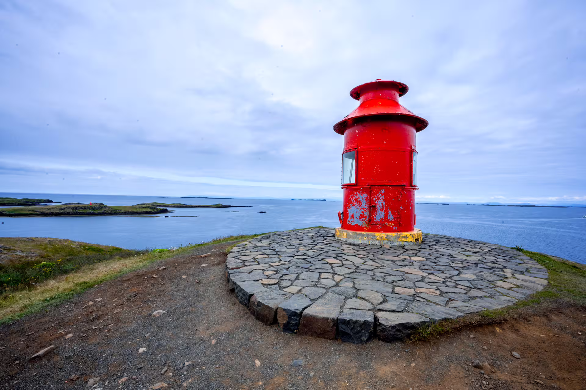 Small red lighthouse on stone platform overlooking Snaefellsnes Peninsula coastline with islands in background