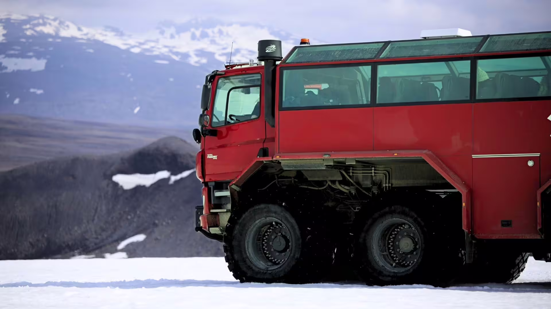 Red Monster truck on glacier, mountains in the background