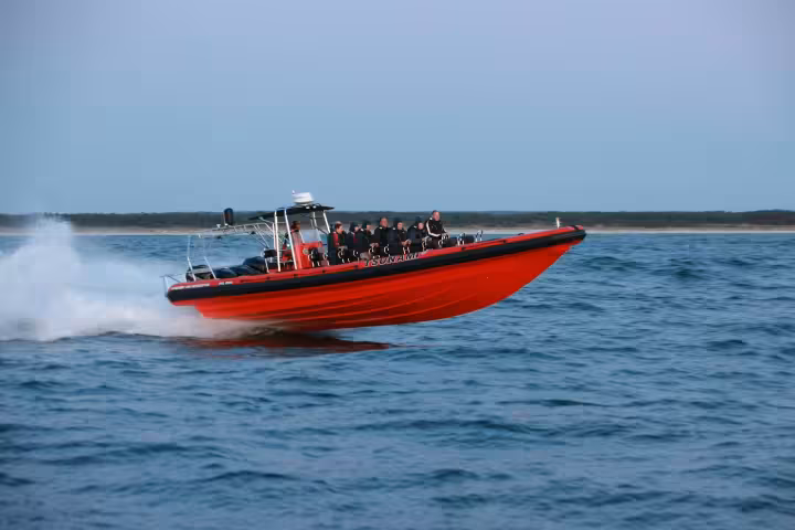 Red RIB speedboat with passengers racing across open ocean waters at high speed