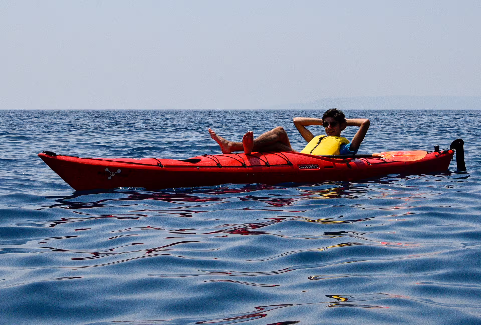 Relaxing on a red sea kayak in calm blue water on the Kardamyli to Stoupa sea kayaking experience, Greece