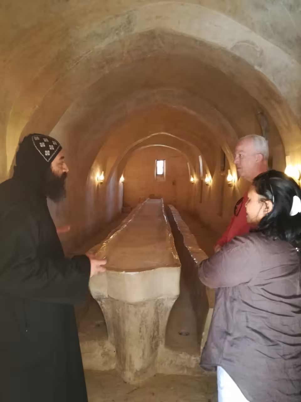 Monk guiding tourists inside ancient stone vaulted crypt at Red Sea monastery, Egypt
