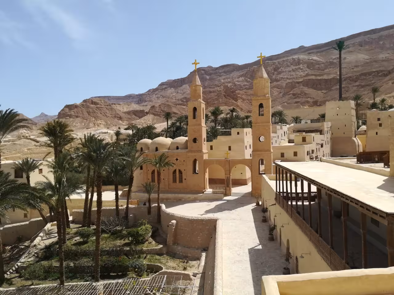 Coptic monastery with twin bell towers and golden crosses nestled against rocky desert cliffs near the Red Sea