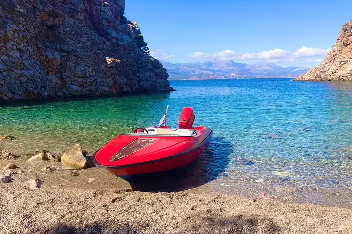 Vibrant red speedboat docked on a secluded beach, surrounded by clear turquoise waters and rocky cliffs.