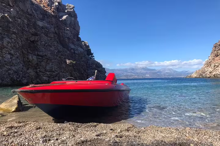 Red speedboat docked on a secluded rocky cove, ready for an adventurous half-day sun and snorkel tour with a skipper.