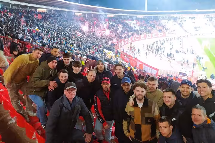 Fans group selfie in Red Star Belgrade stands during a live match, part of a Belgrade football tour with a local