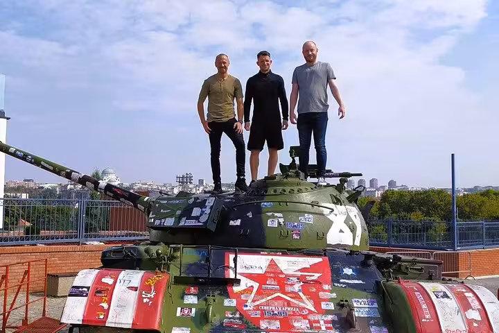 Travelers pose on a Red Star Belgrade tank monument before a live football match tour with a local guide