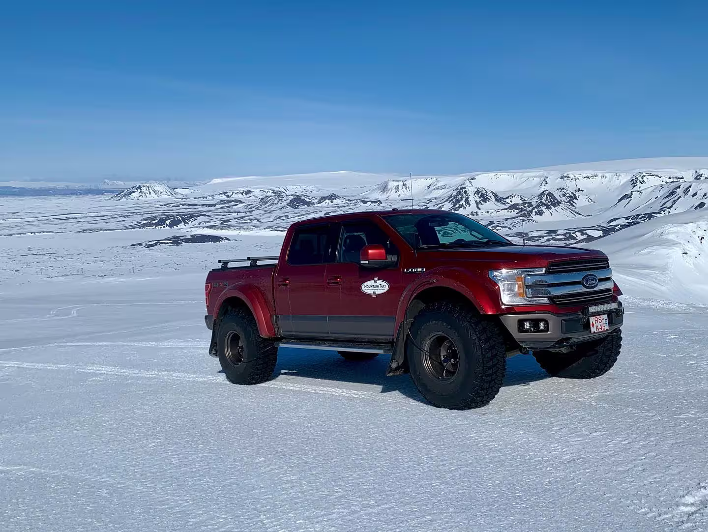 Red lifted Ford F-150 super jeep on Icelandic glacier with snowy mountains in background