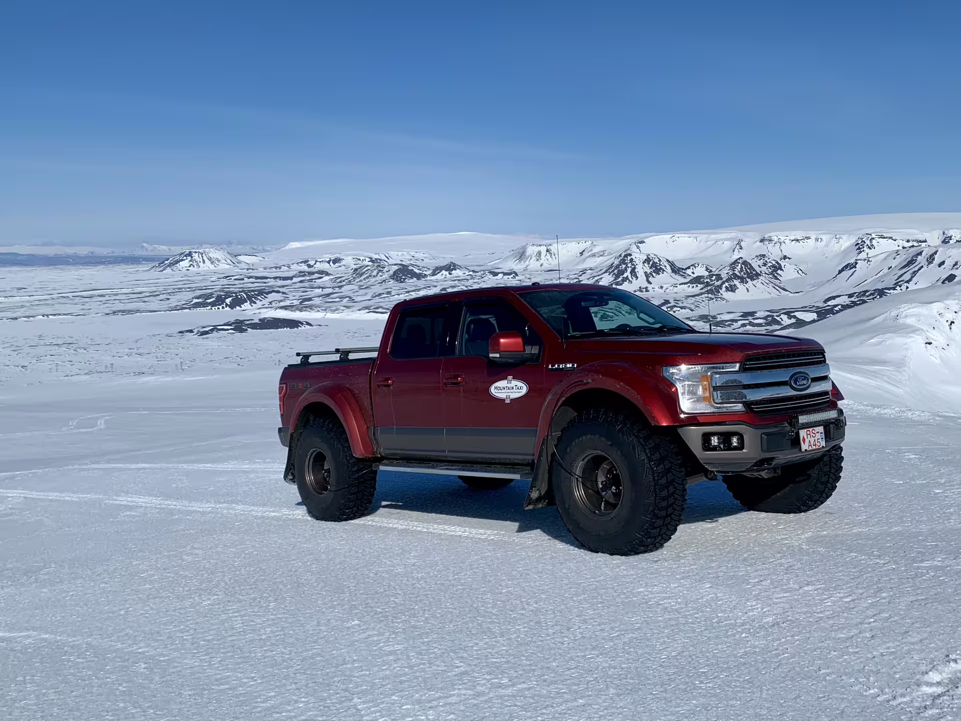 Red lifted Ford F-150 super jeep on a glacier with snow-covered volcanic mountains in Iceland