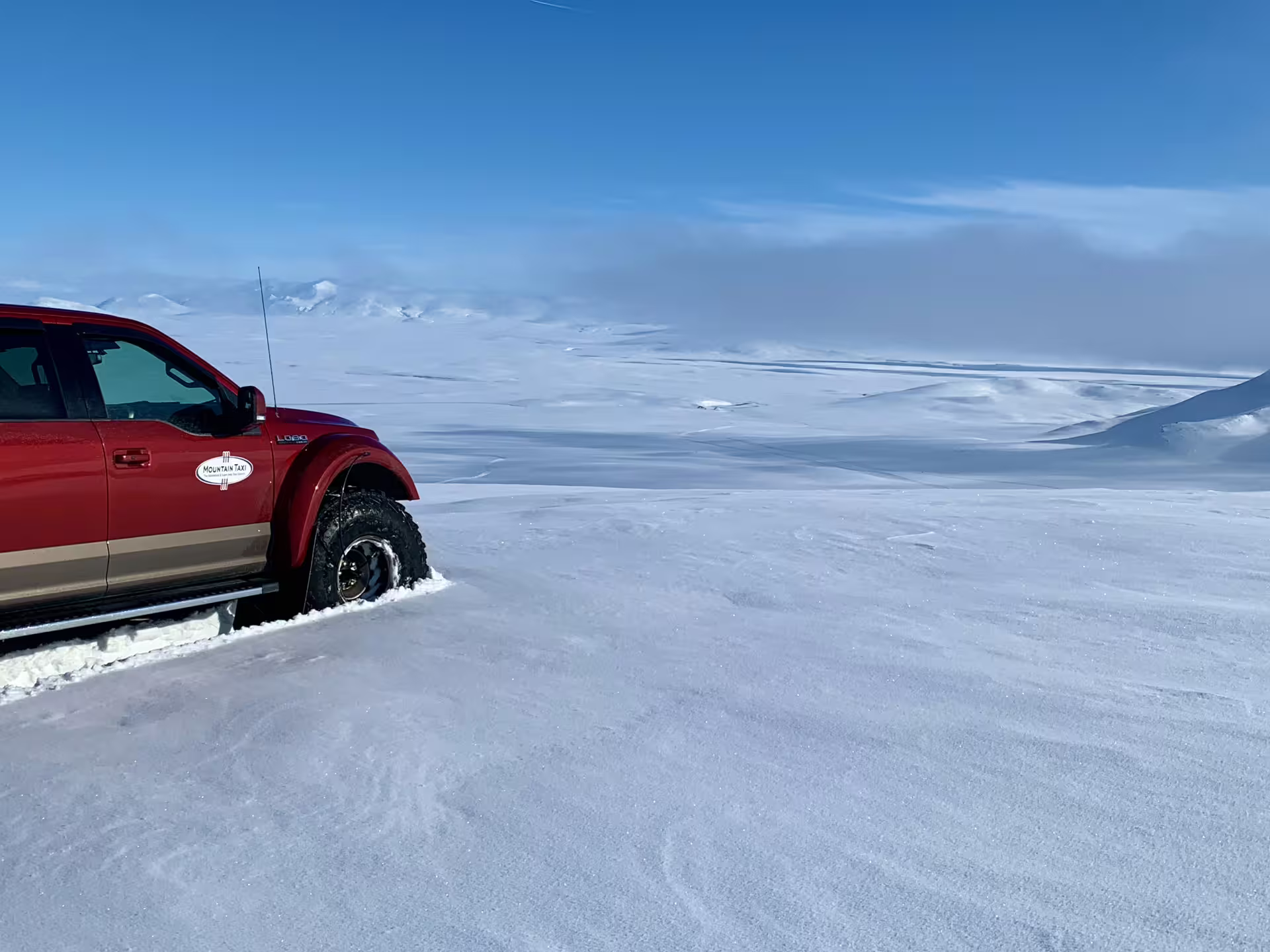 Red super jeep on snowy Iceland highland plateau with vast white landscape and blue sky
