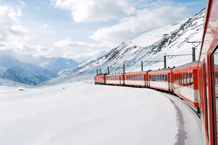 Red train navigating through snow-covered mountains in the Swiss Alps on a scenic journey.