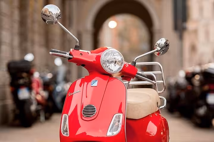 Classic red Vespa motorcycle in Florence with archway backdrop, highlighting stylish Vespa rentals for city tours.