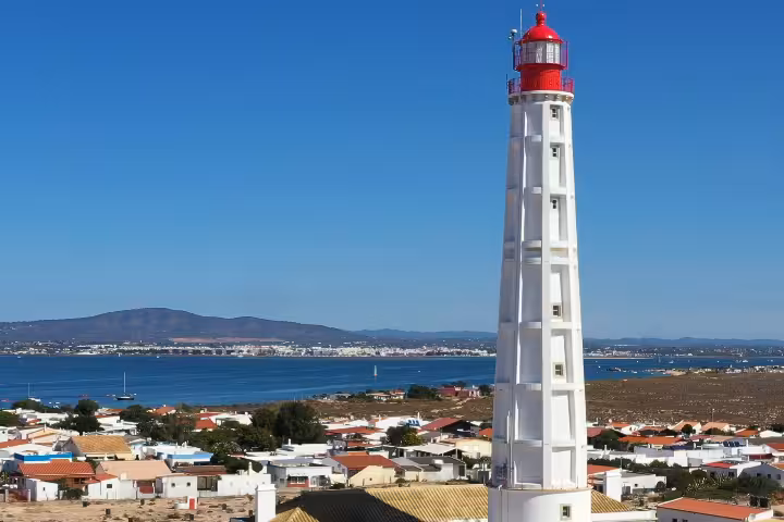 Red and white lighthouse over a seaside town and bay, iconic landmark visit on a group cruise tour