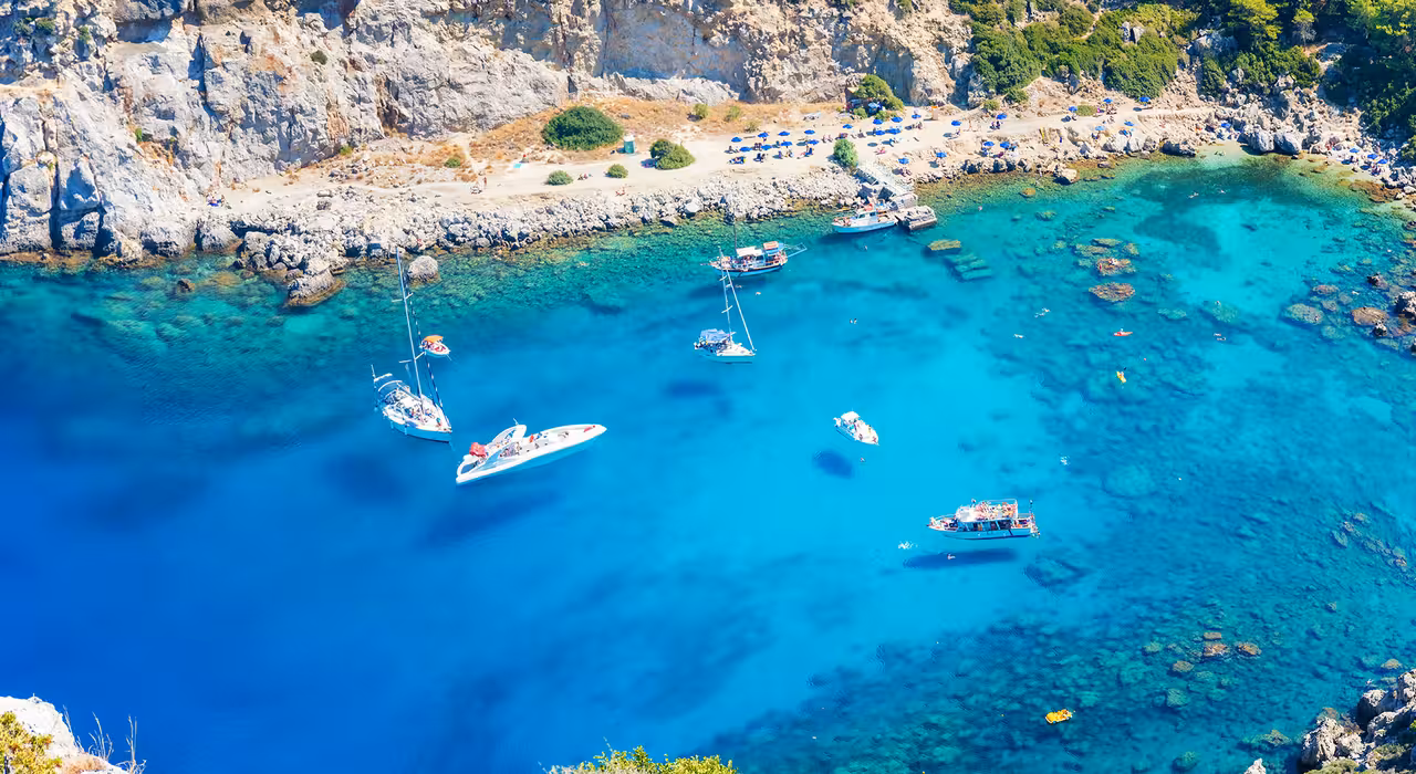 Scenic coastal view with sailboats and yachts floating in clear blue waters near a rocky shoreline on Regal 2700 tour.