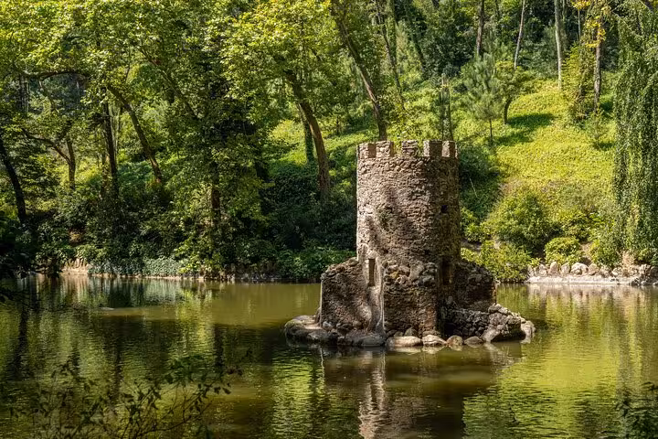 Medieval stone tower reflected in a serene lake surrounded by lush greenery at Regaleira Estate, Sintra day tour.