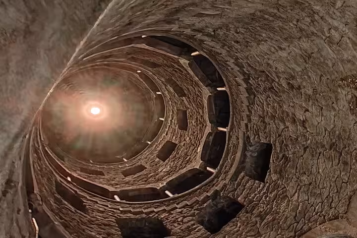 Spiral staircase of the Initiation Well at Quinta da Regaleira, Sintra, with sunlight streaming through the opening above.