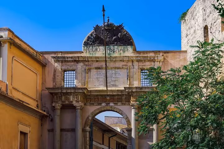Historic Regio Arsenale gate arch in Cagliari, Italy, with ornate stone carvings and blue sky