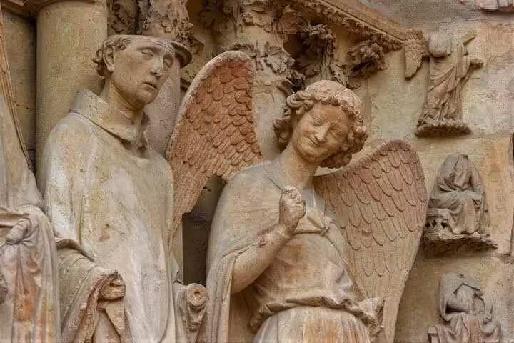Gothic stone sculptures of an angel and saint on Reims Cathedral facade, France