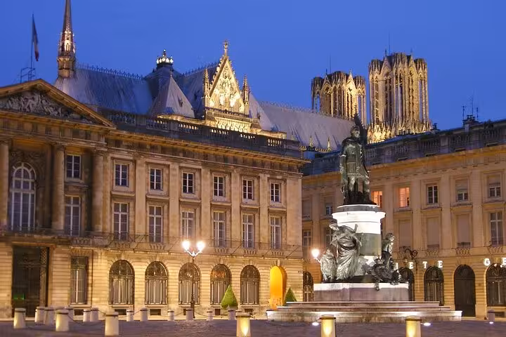 Illuminated Place Royale square with bronze statue and Reims Cathedral towers glowing at dusk