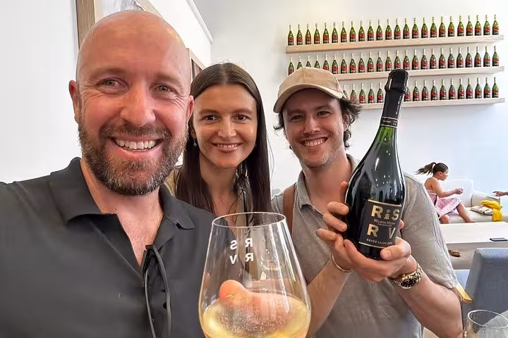 Three smiling visitors holding RSRV champagne bottle and glass during guided tasting tour in Reims