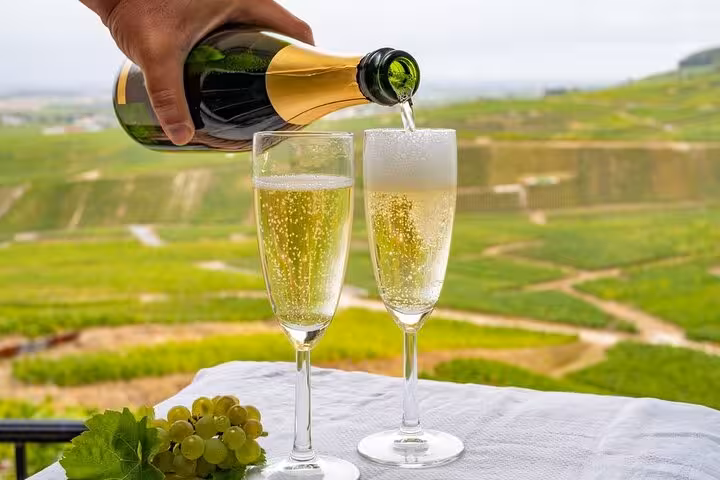 Champagne being poured into two flute glasses on a table overlooking green vineyards in Reims