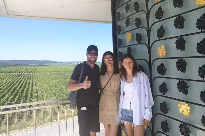 Three tourists posing at a Champagne vineyard overlooking lush green fields in Reims, France