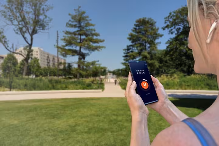 Woman holding smartphone with audio guide app in a sunny urban park during a self-guided walking tour