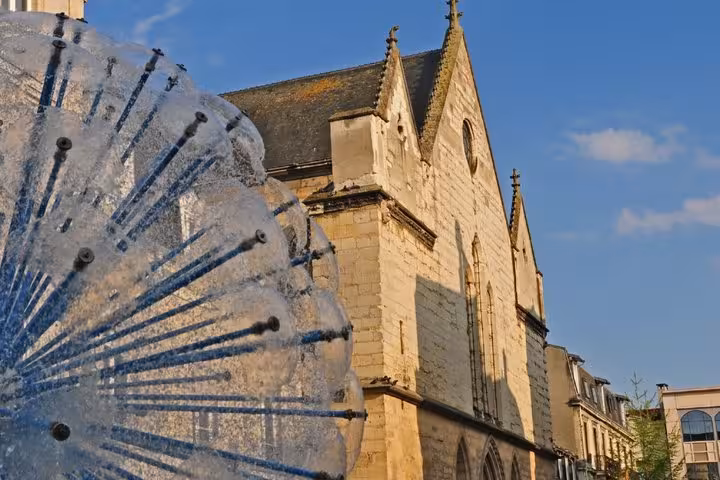 Historic stone church facade in Reims with decorative water fountain in foreground against blue sky
