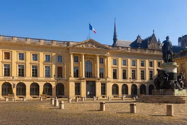 Reims City Hall on Place Royale with French flag and statue on cobblestone square