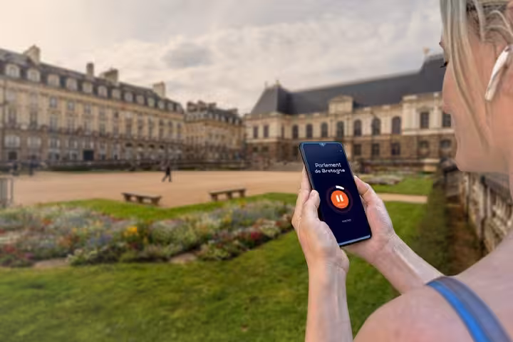 Woman holding smartphone with GPS audio guide app at Parlement de Bretagne in Rennes, France