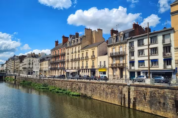 Colorful historic buildings lining the Vilaine River waterfront in Rennes, France under a blue sky