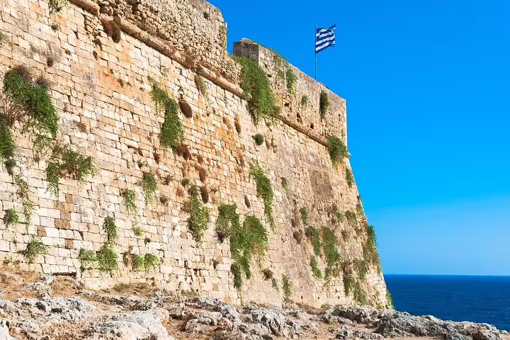 Majestic view of the Rethymno Fortress with Greek flag, showcasing ancient stone walls against a bright blue sky.