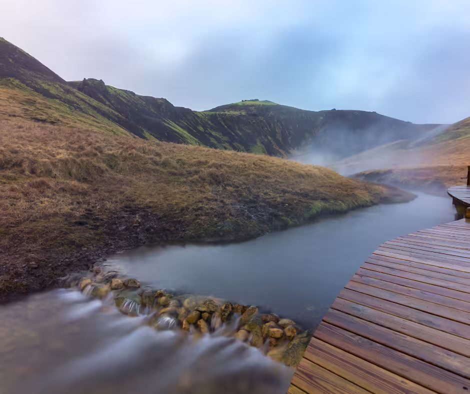 Steaming geothermal hot river winding through green Icelandic hills with wooden boardwalk
