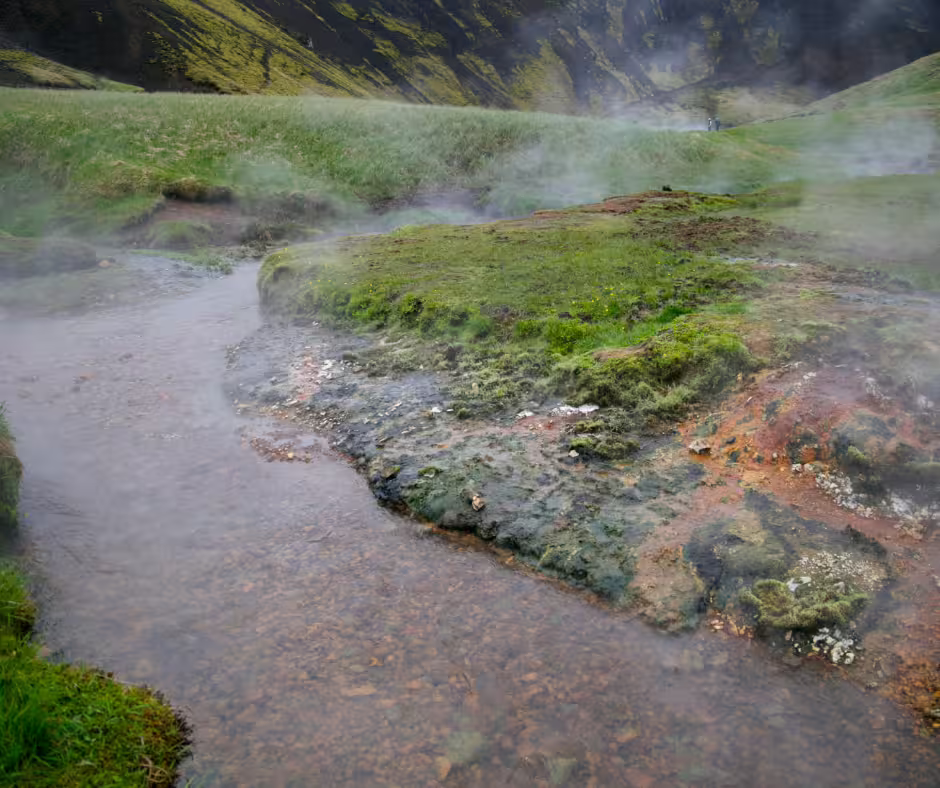 Steaming geothermal hot river with moss-covered rocks and green hills at Reykjadalur, Iceland