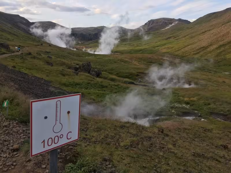 Warning sign showing 100°C temperature near steaming geothermal hot springs in Reykjadalur valley Iceland